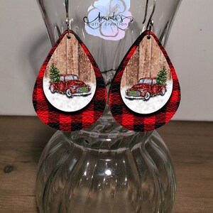 Puede incluir: Pendientes de forma de l&aacute;grima de cuadros de b&uacute;falo rojos y negros con un cami&oacute;n vintage rojo que lleva un &aacute;rbol de Navidad sobre un fondo de madera.