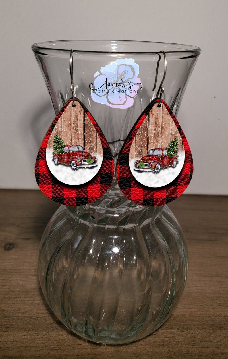 Puede incluir: Pendientes de forma de l&aacute;grima de cuadros de b&uacute;falo rojos y negros con un cami&oacute;n vintage rojo que lleva un &aacute;rbol de Navidad sobre un fondo de madera.