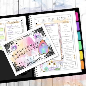 May include: A white spirit board with black lettering and a black border. The board has the letters of the alphabet, numbers 1-7, the words "YES", "NO", and "GOODBYE". A heart-shaped planchette with a rainbow design is on top of the board. The board is on a wooden surface.