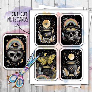 May include: A sheet of cut-out notecards with mystical illustrations. The cards feature a skull, cauldron, butterfly, and eye designs with rainbows, crystals, and celestial elements. The text "CUT OUT NOTECARDS" is visible.