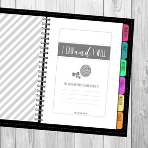以下が含まれることがあります： グレーのストライプの表紙と「I CAN and I WILL」という励みになる言葉が書かれた白黒のプランナー。プランナーには、「Goals」、「Website」、「Social」、「Business」、「Daily」、「Monthly」というタブ付きセクションがあります。