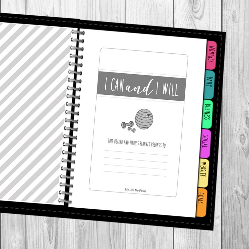 以下が含まれることがあります： グレーのストライプの表紙と「I CAN and I WILL」という励みになる言葉が書かれた白黒のプランナー。プランナーには、「Goals」、「Website」、「Social」、「Business」、「Daily」、「Monthly」というタブ付きセクションがあります。