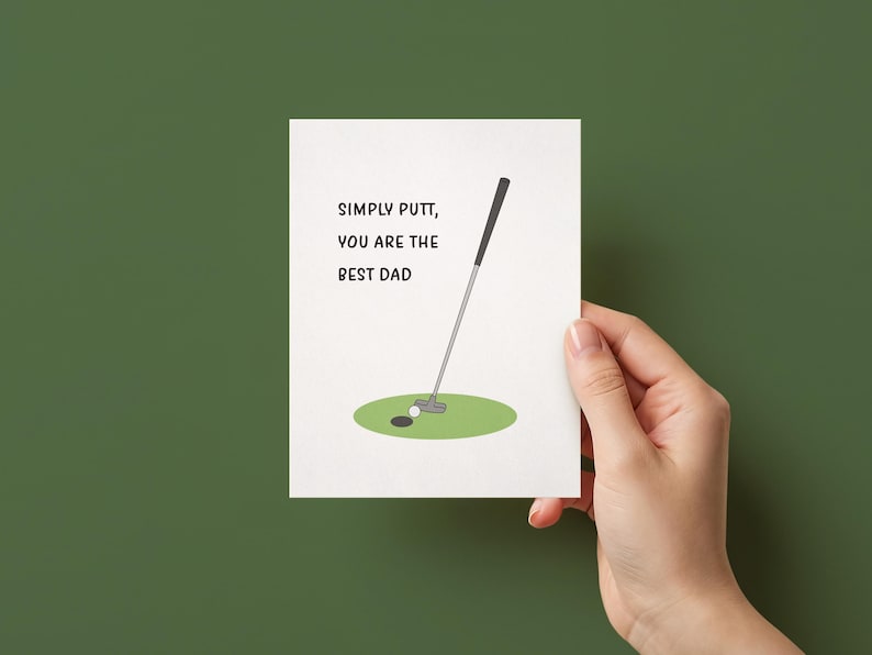 May include: A white greeting card featuring a graphic of a golf putter, a white golf ball, and a green putting green. The text on the card reads, SIMPLY PUTT, YOU ARE THE BEST DAD, printed in a simple black sans-serif font on the left side.