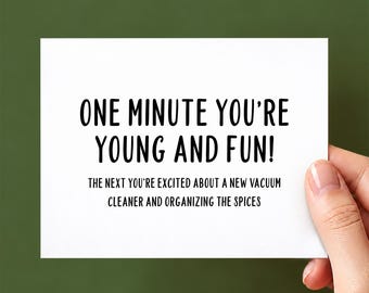 May include: A white rectangular greeting card with black text that reads: ONE MINUTE YOU'RE YOUNG AND FUN! THE NEXT YOU'RE EXCITED ABOUT A NEW VACUUM CLEANER AND ORGANIZING THE SPICES. The card features a clean, minimalist design with bold lettering.