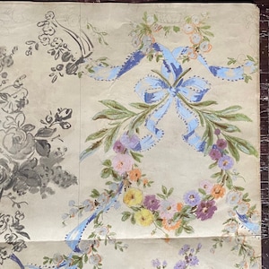 May include: A vintage wallpaper design featuring a floral wreath with blue ribbon bows. The wreath is made up of pink, yellow, and purple flowers. The background is a light beige color.