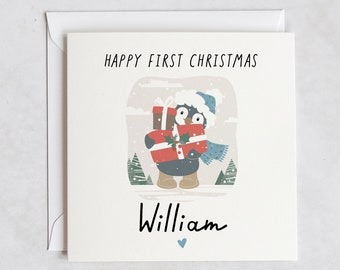 May include: A white card with a penguin illustration holding presents. The card says "Happy First Christmas William" with a small blue heart below the name.