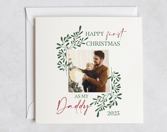 Può includere: Un biglietto di Natale con una foto di un padre e un figlio. Il biglietto ha un design a corona di agrifoglio verde e bianco e il testo "Buon primo Natale come mio papà 2023".