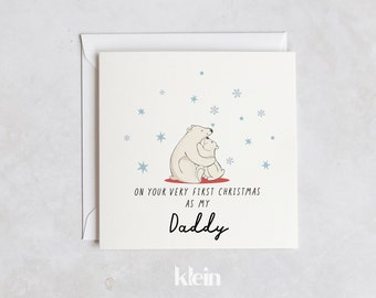 May include: A white card with a drawing of two polar bears hugging. The text on the card reads "On your very first Christmas as my Daddy". The card is from the company "klein".
