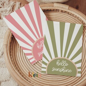 May include: Two greeting cards with a sunburst design. The card on the left is pink with the text "hello sun". The card on the right is green with the text "hello sunshine".