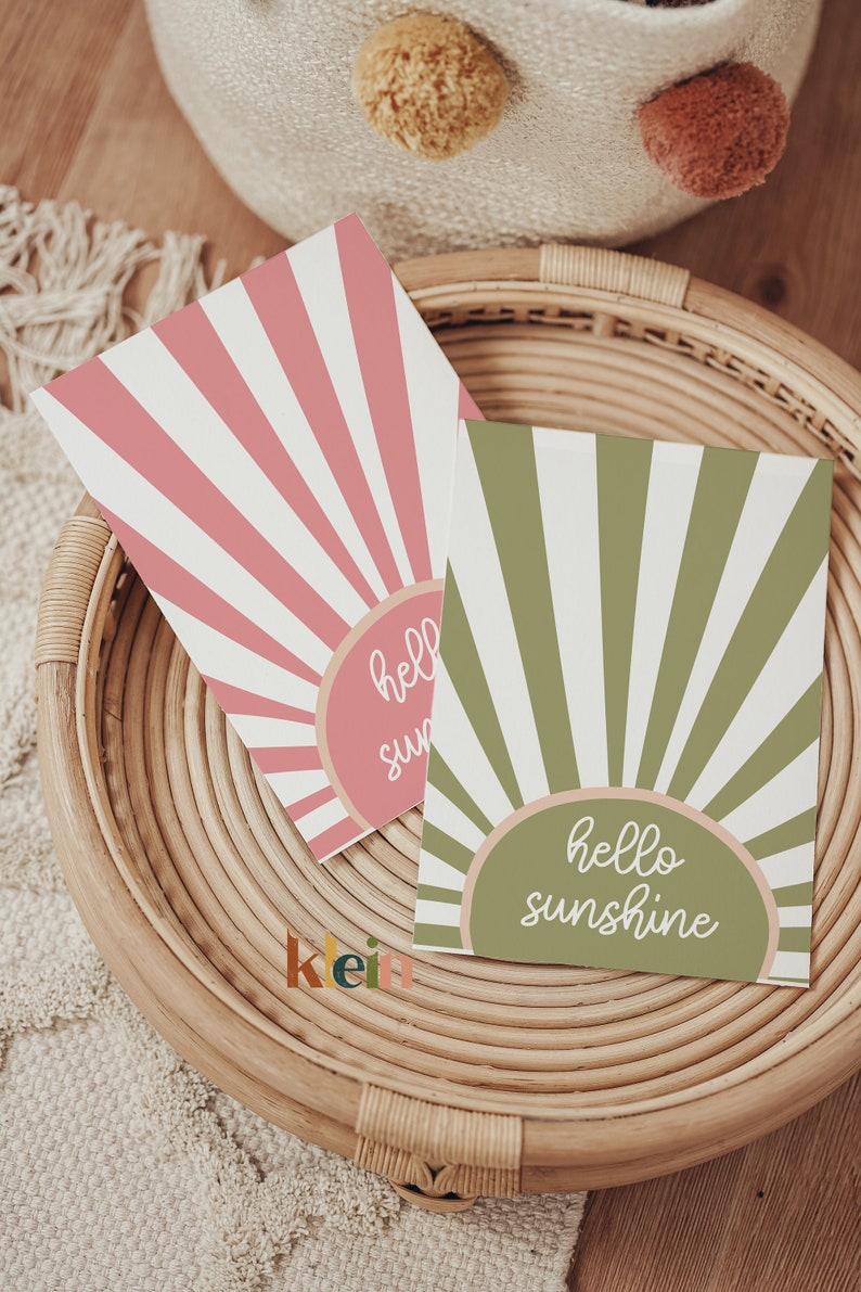 May include: Two greeting cards with a sunburst design. The card on the left is pink with the text "hello sun". The card on the right is green with the text "hello sunshine".