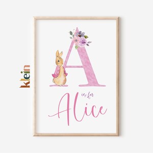 Pode incluir: Uma letra A rosa em aquarela com um design floral e um pequeno coelho marrom vestindo uma jaqueta rosa. O texto "A is for Alice" está escrito abaixo da letra.