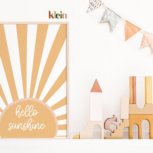 May include: A framed print with a yellow and white sunburst design and the text "hello sunshine" in white script. The print is hanging on a white wall with a wooden shelf below it. The shelf has a small wooden toy castle and a wooden animal figurine on it.