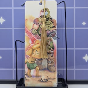 May include: A rectangular bookmark featuring a printed illustration of a green-armored soldier standing behind a yellow dog character. The bookmark has a hole at the top with a gold-colored tassel attached and is displayed in a black metal stand.