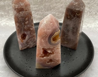 May include: Three pink and purple agate crystal points with natural druzy formations and cavities. The points are arranged on a black plate.