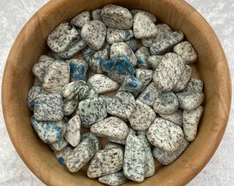 May include: A bowl filled with blue and white kyanite tumbled stones. The stones are smooth and polished, and they have a variety of shapes and sizes.