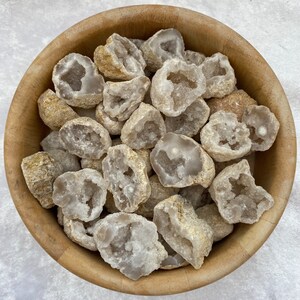 May include: A wooden bowl filled with white and brown agate crystal geodes. The geodes are various sizes and shapes, with some having a more pronounced crystal formation.