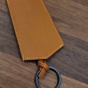 May include: A brown leather key chain with a green stitched border and a silver metal ring. The key chain has a loop for attaching keys.