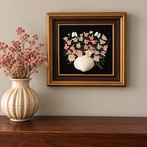May include: A square wall art piece in a dark brown and gold frame featuring a seashell arrangement on a black background. The art depicts a white seashell vase filled with pink, white, and cream shell flowers and green foliage accents.