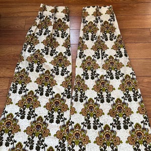 May include: Two vintage floral patterned curtain panels. The curtains feature a repeating pattern of brown, green, and tan floral designs on an off-white background. The panels are folded and appear to be made of a textured fabric.