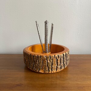 May include: A wooden nutcracker set featuring a natural wood bowl with a bark-like exterior and a light brown interior. The set includes a silver nutcracker and three silver nut picks. The bowl is approximately 6 inches in diameter.
