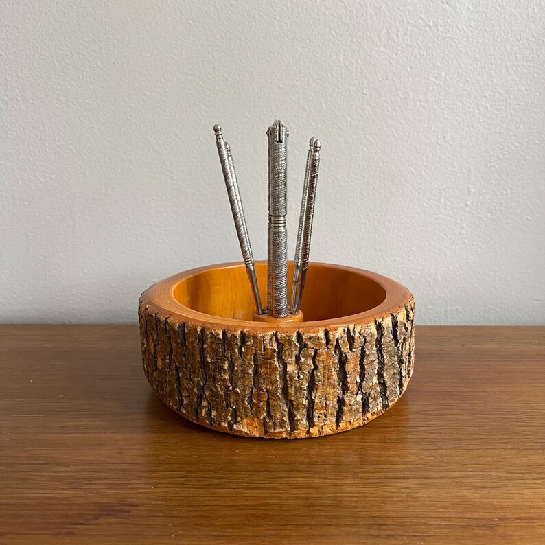 May include: A wooden nutcracker set featuring a natural wood bowl with a bark-like exterior and a light brown interior. The set includes a silver nutcracker and three silver nut picks. The bowl is approximately 6 inches in diameter.
