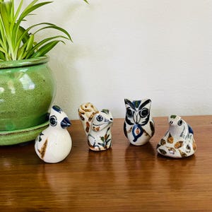 May include: Four ceramic animal figurines: a bird, a squirrel, an owl, and a frog. The bird is white with blue and brown accents. The squirrel has brown and tan markings. The owl is white with black and blue details. The frog is white with brown and blue spots.