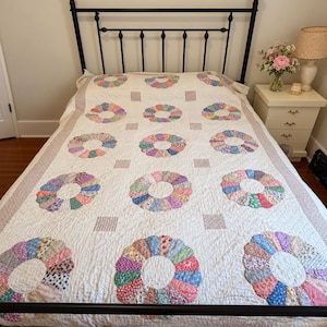 May include: A white bed quilt featuring a repeating pattern of circular floral motifs made from various multicoloured patterned fabric segments. The quilt includes small square accents between the circles and a wide border with a subtle print.