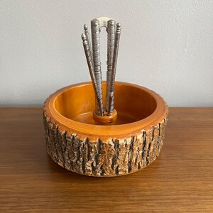 May include: A vintage nutcracker set featuring a wooden bowl with a bark-like exterior and a set of silver-toned nutcrackers. The bowl has a warm, orange-brown interior. The nutcrackers are arranged in the center of the bowl.