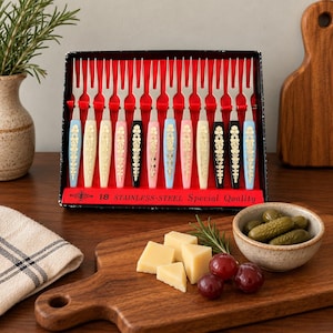 May include: A set of twelve stainless steel appetizer forks arranged in a black box with red lining. The handles feature colorful pastel and black plastic with gold floral patterns. The box text reads 18 STAINLESS-STEEL Special Quality.