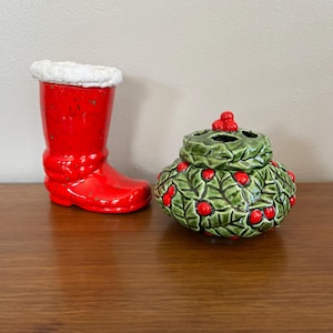 Peut inclure: Un botte de Noël en céramique rouge avec une bordure en fausse fourrure blanche est à côté d'un pot en céramique verte décoré de feuilles de houx et de baies rouges. Le pot a un couvercle avec un groupe de baies de houx.