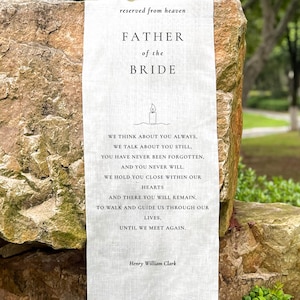 May include: A white linen banner with the text "reserved from heaven" and "Father of the Bride." The banner includes a poem and is displayed outdoors, resting against a stone.