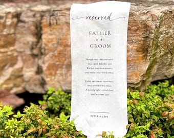 May include: A white fabric sign with the words "reserved" and "FATHER of the GROOM" in elegant script. The sign includes a poem and the name "PETER A ZEPF" at the bottom. The sign is displayed outdoors.