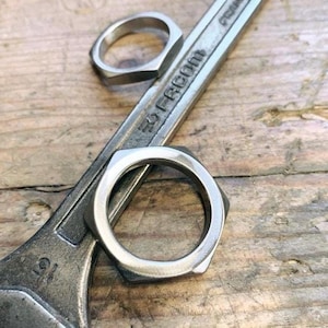 Peut inclure: Deux anneaux en métal argenté, l'un de forme hexagonale et l'autre de forme arrondie, sont placés sur une clé à molette. La clé à molette est en métal et porte l'inscription "30 FROM".