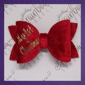 May include: A red velvet bow with gold lettering that says "My First Christmas".