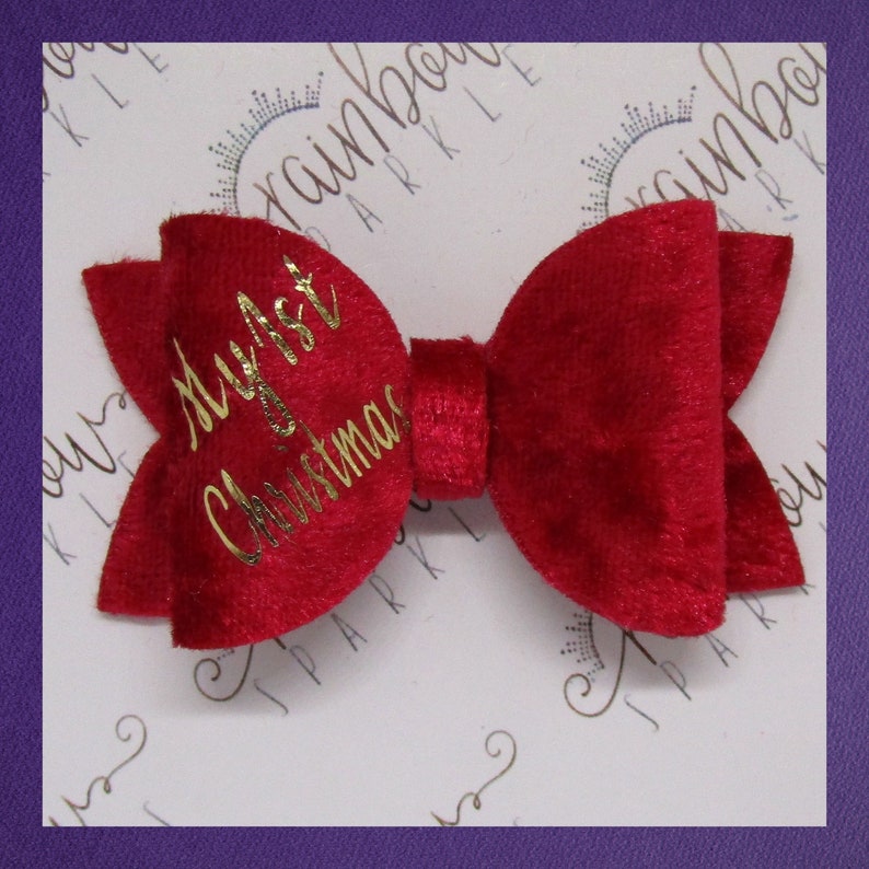 May include: A red velvet bow with gold lettering that says "My First Christmas".