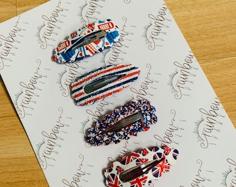 Può includere: Set di quattro fermagli per capelli con diversi design. I fermagli sono rosso, bianco e blu con una varietà di motivi, tra cui una cabina telefonica di Londra, strisce e glitter. I fermagli sono su uno sfondo bianco con il testo "Rainbow Sparkles" ripetuto.