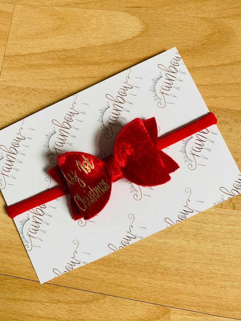 May include: Red velvet bow with a gold inscription that reads "It's a Christmas" on a white background with a repeating pattern of the words "rainbow sparkles".