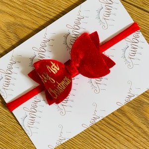 May include: Red velvet bow with a gold inscription that reads "My 1st Christmas". The bow is attached to a red elastic headband.