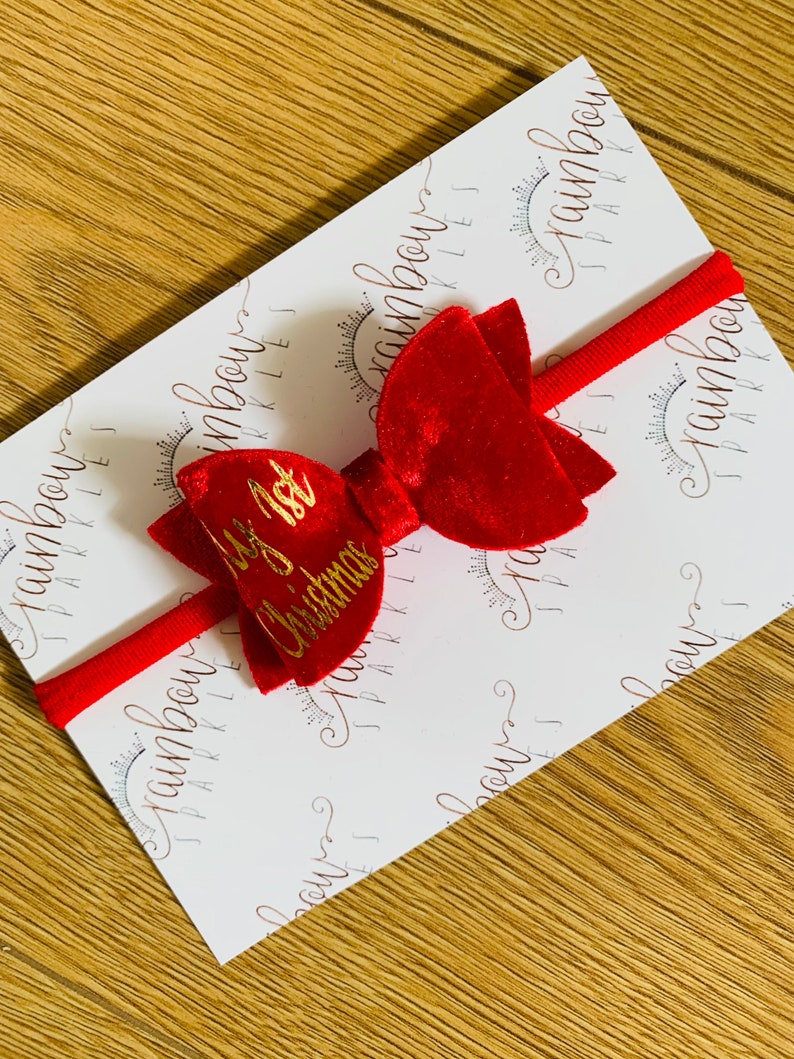 May include: Red velvet bow with a gold inscription that reads "My 1st Christmas". The bow is attached to a red elastic headband.