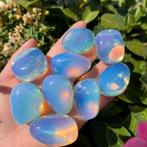 May include: A collection of eight iridescent opalite tumbled stones. The stones are smooth and polished, with a variety of colors, including blue, green, and pink.