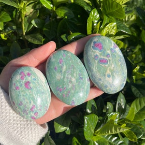 May include: Three green and pink tumbled stones with a marbled pattern. The stones are smooth and polished.