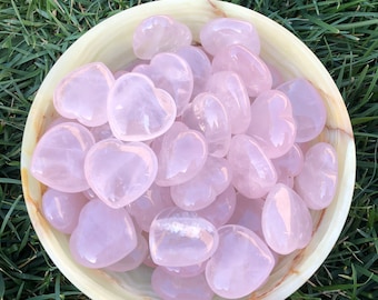 May include: A bowl filled with pink rose quartz heart-shaped stones. The bowl is made of a light green material and has a smooth, polished finish.