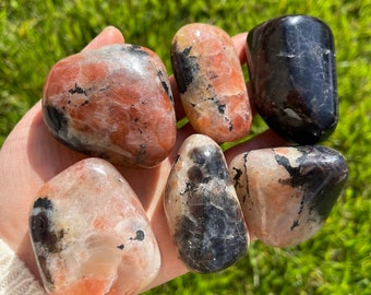 May include: Six tumbled stones with a mix of pink, orange, and black colors. The stones are smooth and have a natural, polished look.