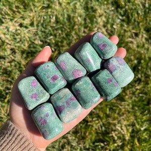 May include: A collection of eight green and pink tumbled stones. The stones are smooth and polished, with a variety of shapes and sizes.