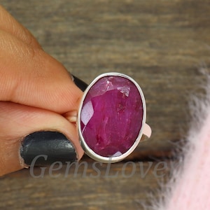Op de afbeelding: Een zilveren ring met een grote, ovale robijn. De robijn is diep rood van kleur en heeft een facetgeslepen vorm.