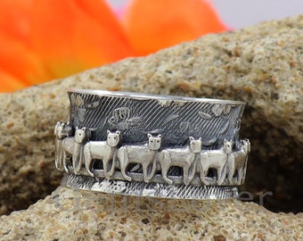 May include: A silver ring with a band of cats walking around the ring. The cats are in a circle and are all facing the same direction. The ring is on a rock.