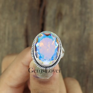 Peut inclure: Une bague en argent avec une grande pierre pr&eacute;cieuse ovale et iris&eacute;e. La pierre pr&eacute;cieuse a une base bleu clair avec des couleurs arc-en-ciel.