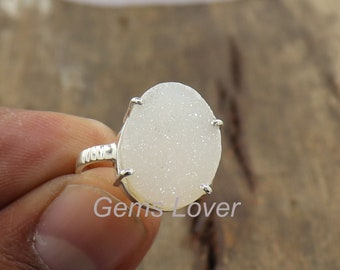 May include: White gemstone ring with a silver setting. The gemstone is oval shaped and has a sparkly, textured surface.