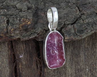 May include: A silver pendant featuring a raw pink ruby gemstone. The ruby is set in a silver bezel and has a natural, irregular shape.