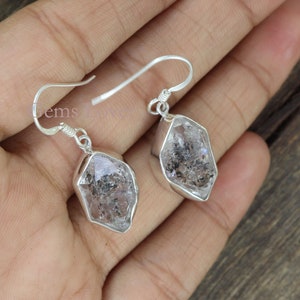 May include: A pair of silver earrings with clear quartz crystal drops. The crystals are faceted and have a geometric shape.